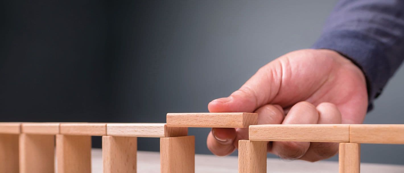 Eine Männerhand baut eine Holzbrücke aus Miniaturklötzchen.
